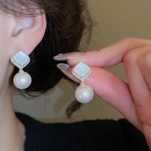 Detail of silver pearl drop earrings with zircon flower design on a hand and ear model
