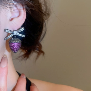Dettaglio di orecchini a fiocco d'argento con pendente di ghianda viola indossati dalla modella