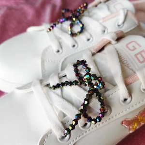 Detail von bunten Kristallperlen und gesticktem Schmetterling auf weißem Leder-Sneaker