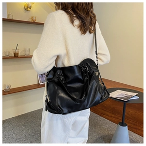 Close-up of a large black leather tote bag worn by a model in a minimalist modern cafe setting