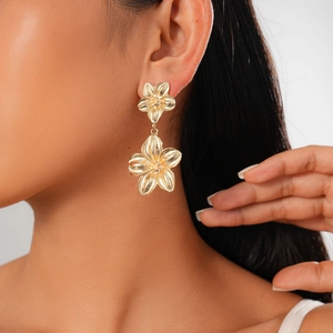 Close-up of model wearing golden double flower earrings with textured metallic petals