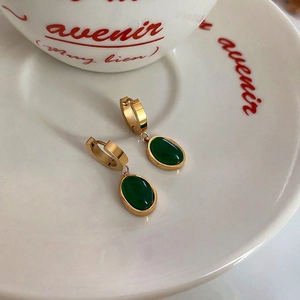 Elegant vintage gold-tone emerald green oval drop earrings displayed on a white saucer