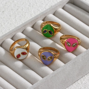 Detailed macro view of four golden alien rings with colorful enamel on a gray display tray
