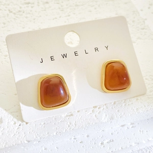 Detail of amber resin earrings in gold frames displayed on a white textured stand