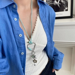 Détail d'un collier mousqueton cœur argenté avec fil bleu et breloques sur cordon vert