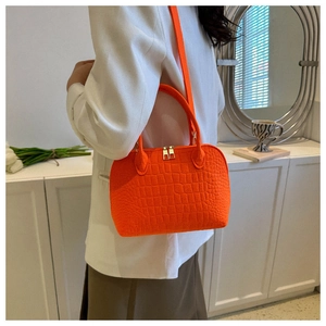 Detail view of bright orange shell bag with crocodile texture and gold dual zippers