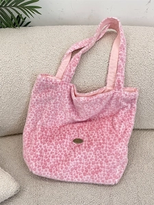 Sac fourre-tout en peluche léopard rose avec logo Sazakka en métal sur un canapé