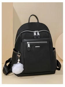 Detail of black commute backpack with silver zippers and a decorative white pompom