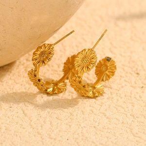 Détail de créoles marguerites en acier inoxydable plaqué or 18K sur tissu beige