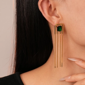 Close-up of golden rectangular earrings with green gemstone and long metal tassels