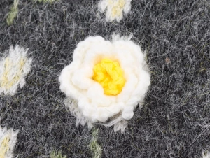 Dettaglio della decorazione floreale 3D bianca e gialla su un cardigan in maglia grigia