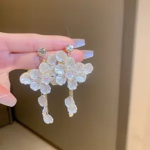 Détail de boucles d'oreilles fleur blanche avec cristaux et longues pampilles dorées