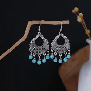 Detail of bohemian drop earrings with blue beads and hollow metal texture on wooden branch
