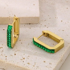 Macro detail of gold rectangle earrings with green baguette stones on light stone
