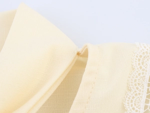 Close-up of the delicate white lace trim and textured cotton-linen fabric in pale yellow