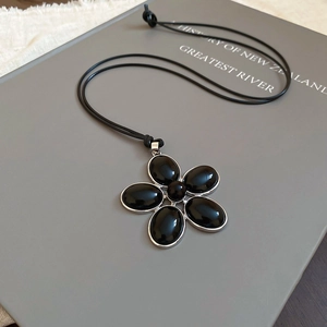 Detailed view of resin flower pendant with black petals and silver metallic edge on a book