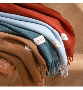 Detail showing various solid color cashmere-like scarves with fringe on a wooden chair