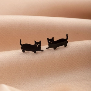 Macro shot of cute black cat stud earrings on soft beige silk background
