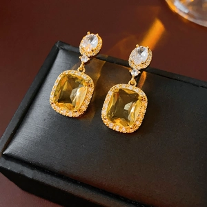 Macro shot of square yellow gemstone earrings with zircon inlay on luxury black leather