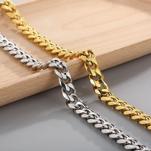 Close-up of polished gold and silver Cuban link chains on a minimal wooden display