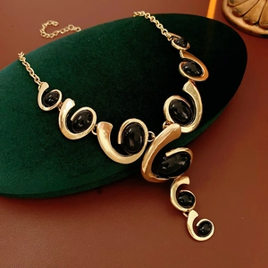 Detailed shot of golden swirl necklace with black oval gemstones on velvet