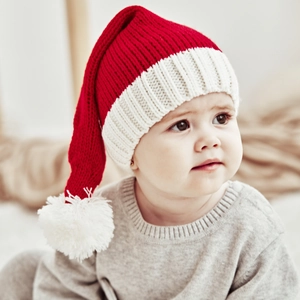 Close-up of a baby wearing a red and white knitted Christmas hat with a soft yarn pom-pom