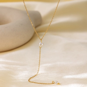 Minimalist Y-shaped gold plated stainless steel necklace with white pearls on silk background