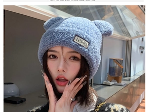 Detail of light blue fuzzy knit hat with bear ears and logo patch in soft plush fabric