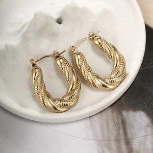Macro shot of gold-finished twisted rope hoop earrings resting on a white textured plate