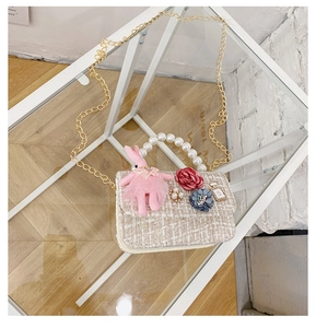 Detail of tweed crossbody bag featuring pearl handle, metal chain and plush bunny charm
