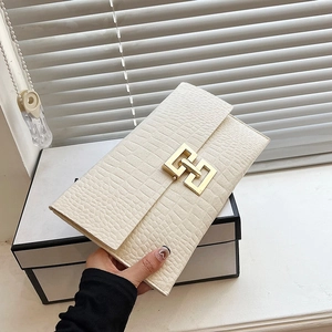 Chic cream crocodile pattern clutch bag with gold geometric clasp held by hand