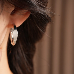 Close-up of stylish polished metal hoop earrings worn by a model in warm light
