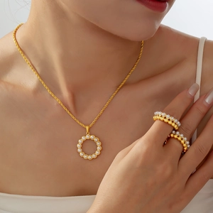 Golden pearl jewelry set with a round pendant necklace and layered beaded rings on a model