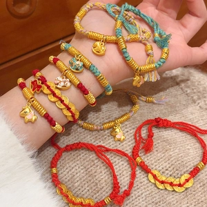 Macro shot of red braided rope bracelet with golden pony and enamel charms for prosperity