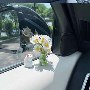 Close-up of mini rabbit figurine and jasmine glass vase on car dashboard with sunlight