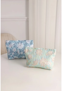 Dettaglio di trousse in jacquard con ricamo floreale ed etichetta tessuta del marchio