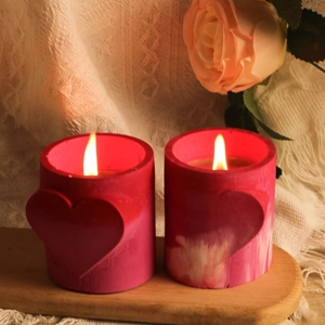 Detail van twee roze stompkaarsen met hartreliëf op houten dienblad met warm kaarslicht