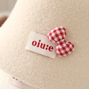 Close-up of soft beige lamb wool bucket hat featuring a red plaid bow and woven brand tag