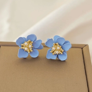 Macro detail of sky blue flower earrings with golden pearl center on leather display