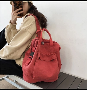 Red canvas backpack shown on shoulder highlighting the large front pocket and casual style