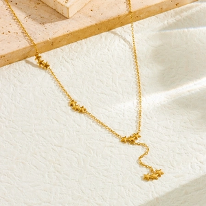 Detail of gold Y-shaped necklace with star pendants on a beige textured surface