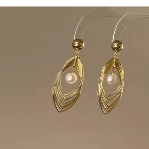 Detail of layered gold teardrop earrings with a white pearl drop and geometric metal frame