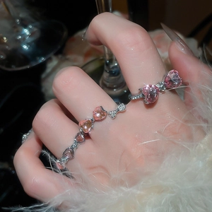 Close-up of sparkling pink heart-shaped bow rings set on a soft feather background