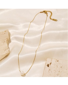 Detail of a round white pearl pendant on a gold chain over elegant cream satin