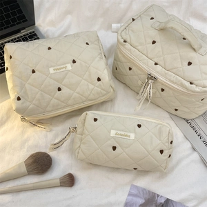 Detailed set of three beige quilted heart pattern cosmetic bags for travel organization