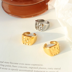 Three gold and silver square hammered metal open rings on elegant textured paper background
