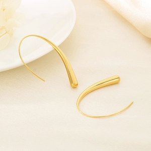 Detailed view of gold teardrop earrings on a textured beige background with white decor