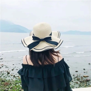Straw sun hat with large brim and black bow detail shown in seaside setting