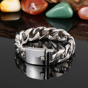 Chunky stainless steel Cuban link bracelet for men on a black reflective mirror surface