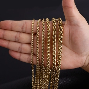 Various sizes of golden stainless steel dragon bone chains held in hand against dark background